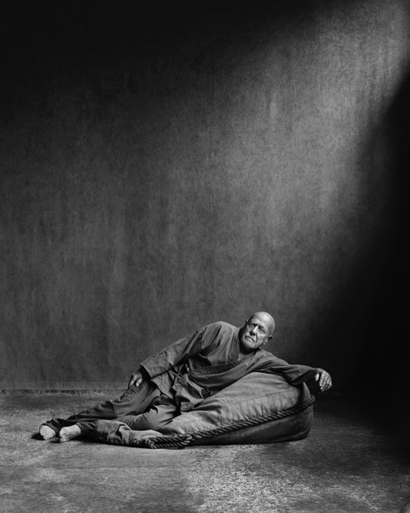 Monochromatic portrait of a bald, mature man reclining on a beanbag chair in a photo studio with directed spotlight.