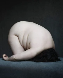 Curled nude person with dark hair tucked downward on a textured grey surface
