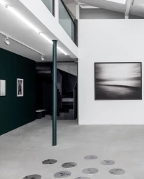 Monochrome interior view of a contemporary Milan gallery space with framed artwork on white and dark walls, captured by photographer Stephan Vanfleteren.