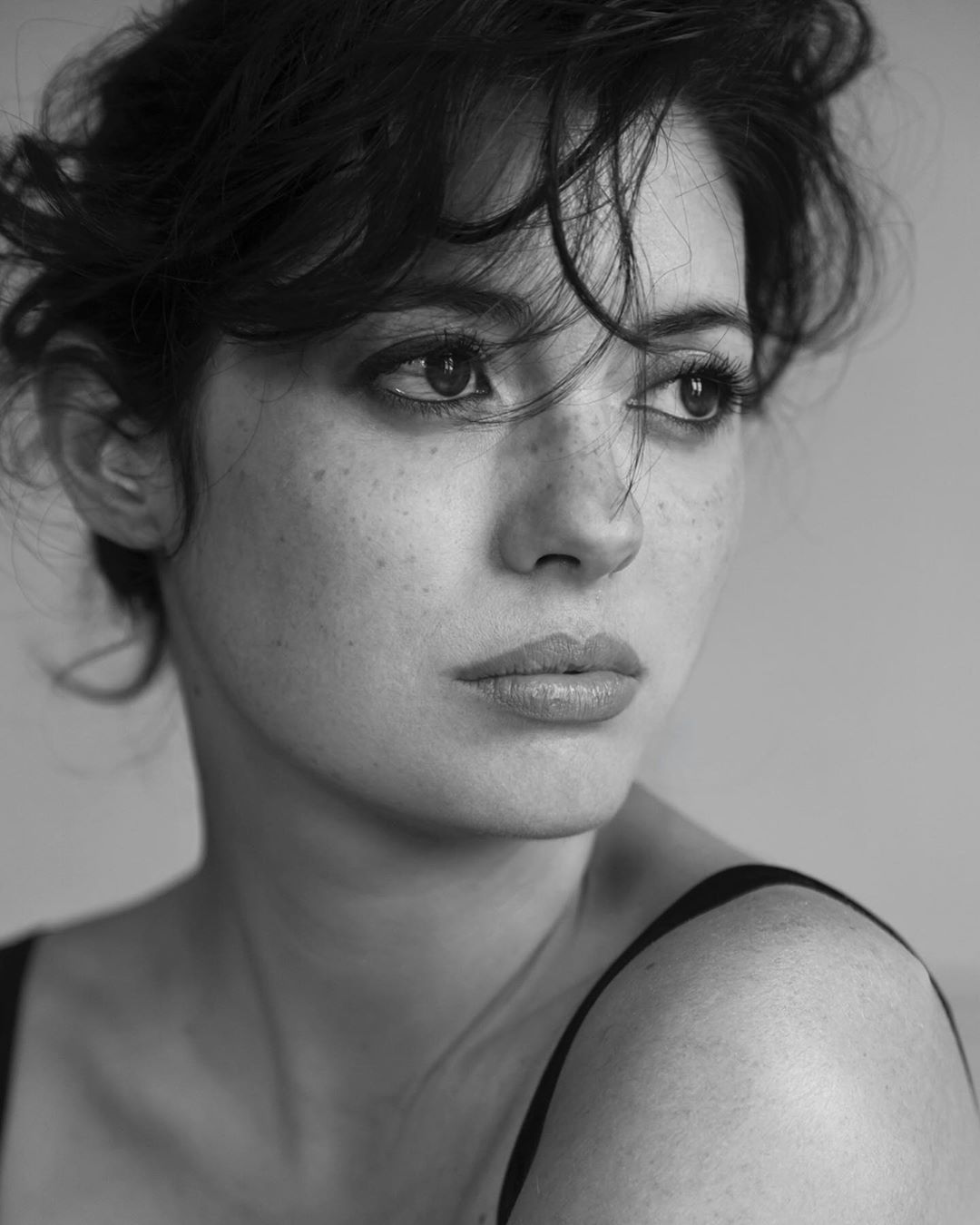 Black and white portrait of a woman with dark, short hair and freckles, gazing away from the camera in a photo studio.