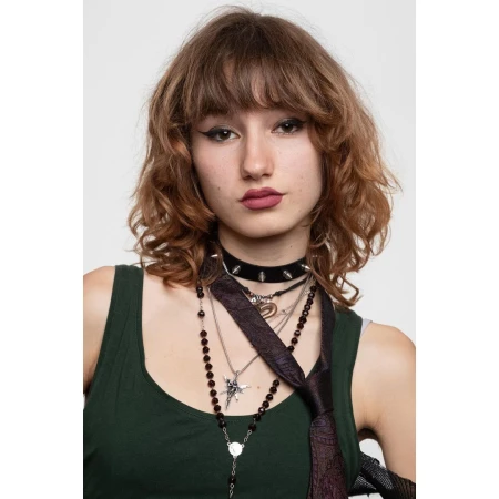 Portrait of a young adult woman with auburn curly hair, dark green top, and multiple necklaces against a white studio backdrop.