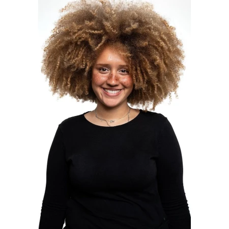 Portrait of a smiling woman with voluminous curly hair and freckles wearing a black long-sleeve top against a white background.