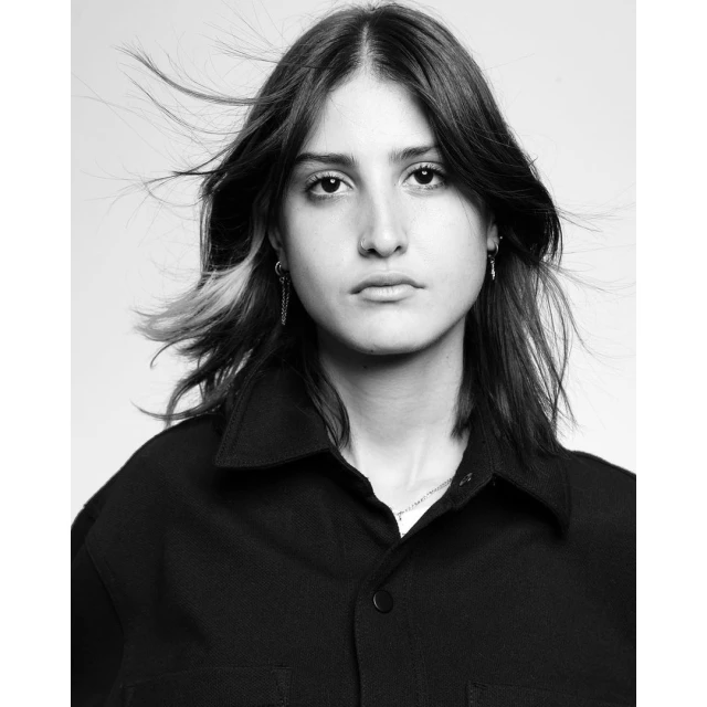 Black and white portrait of a young adult female with dark hair and a black collared shirt looking directly at the camera indoors.