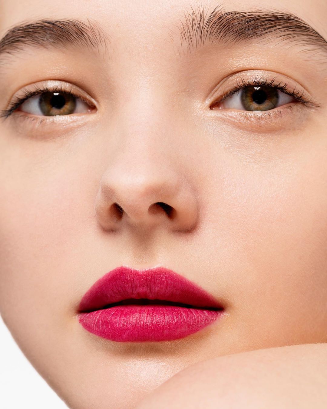 Close-up beauty portrait of a young woman wearing vibrant pink lipstick against a seamless white background