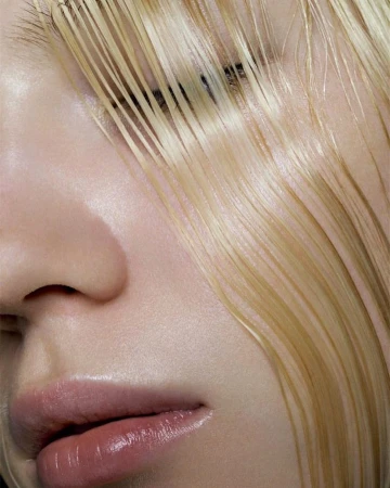 Close-up portrait of a person with wet blonde hair falling across their face, glossy lips, and smooth skin.