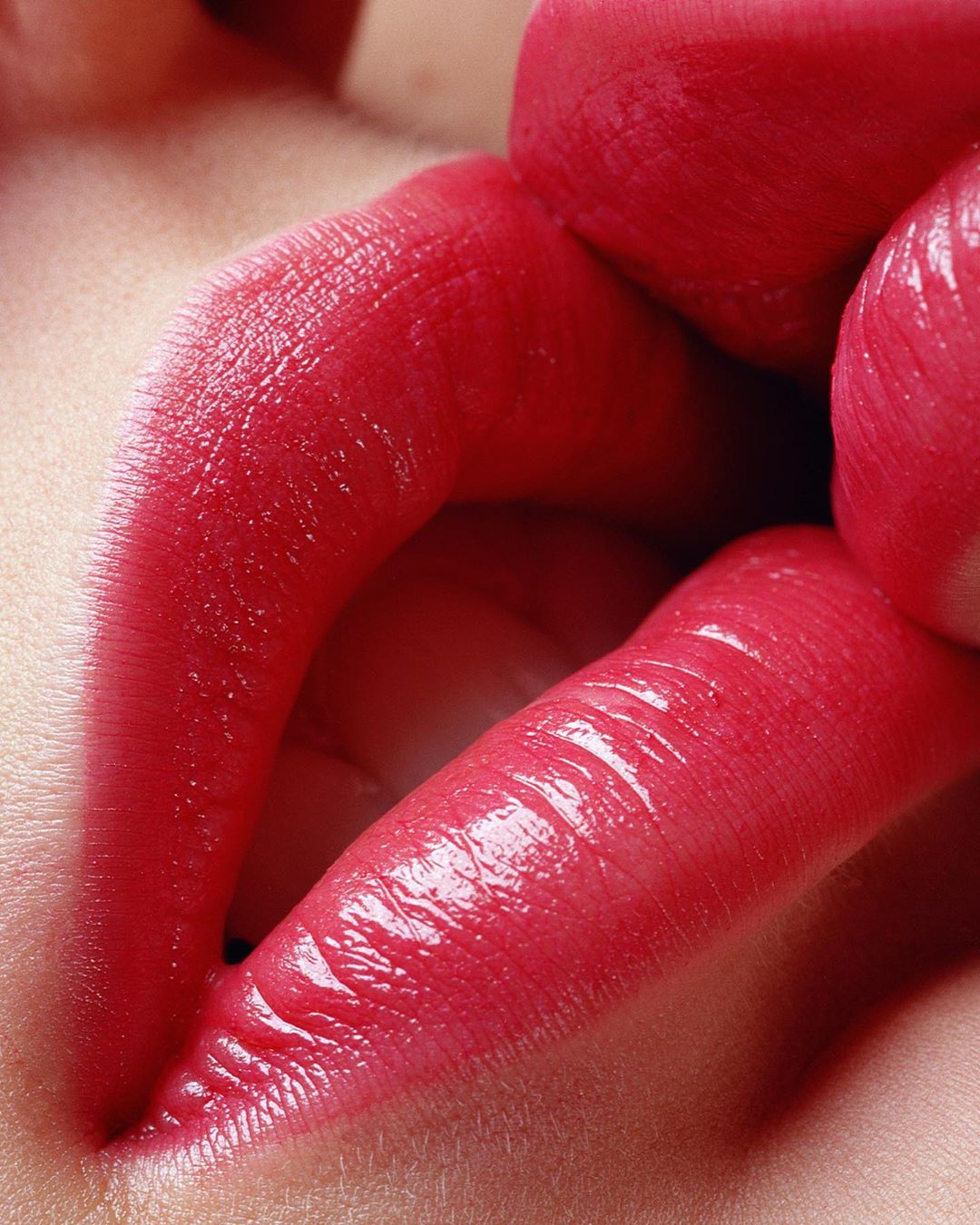 Macro shot of a woman's red lips with glossy lipstick. Close-up of the upper and lower lips, showing the texture and color of the makeup.
