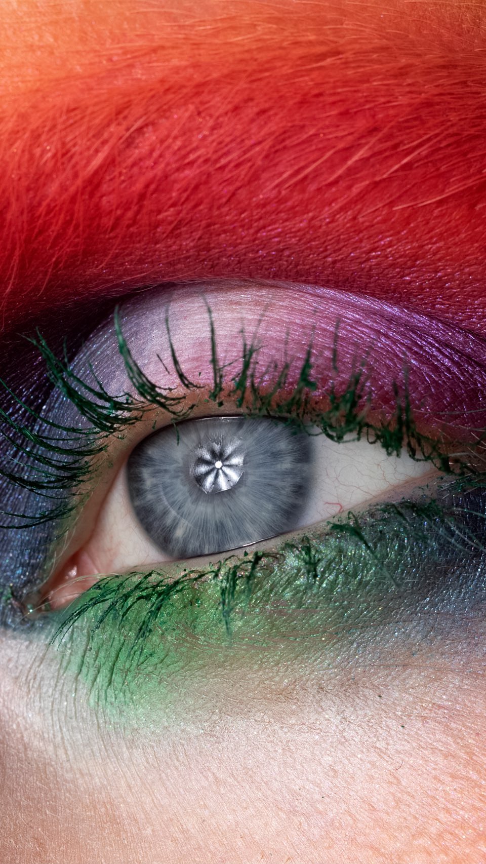 Extreme close-up of a human eye with rainbow-colored eyebrow and vibrant green mascara on the eyelashes in vertical composition.