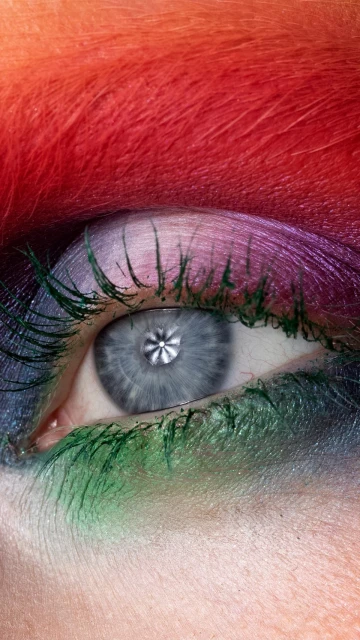 Extreme close-up of a human eye with rainbow-colored eyebrow and vibrant green mascara on the eyelashes in vertical composition.