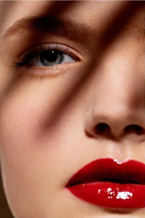 Extreme close-up portrait of a woman face featuring glossy red lips and striking eye makeup photographed by Stephane Coutelle