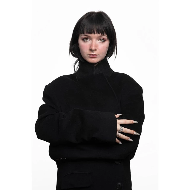 Portrait of a young adult woman with black hair in a black jacket against a white backdrop, looking directly at the camera.