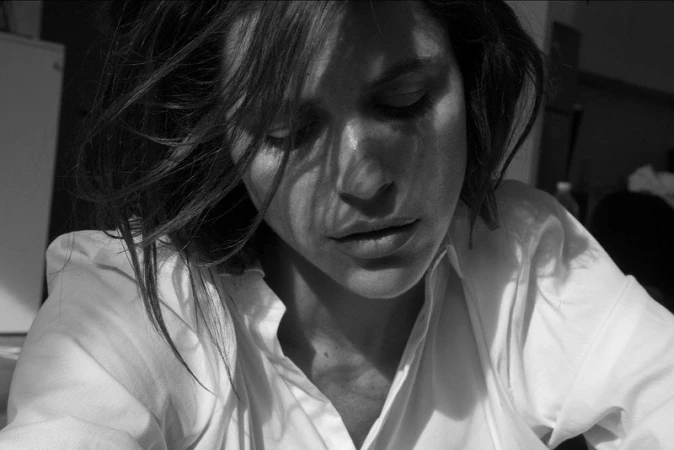 Close-up monochrome portrait of a woman with tousled dark hair wearing a white collared shirt, captured by Stephane Coutelle.