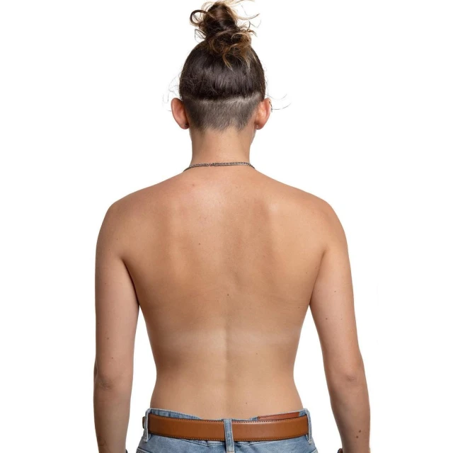 Woman's bare back, turned away from camera, hair in messy bun. Tan skin with tan line on her back. Wearing blue denim jeans and a brown belt.