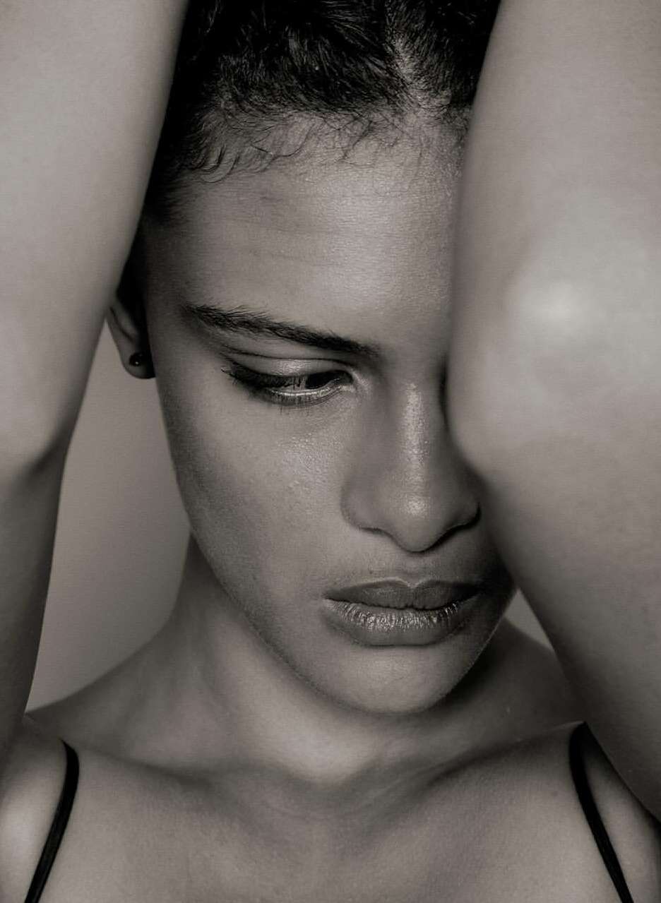 Close-up monochrome portrait of a woman with her arms raised framing her face by photographer Stephane Coutelle