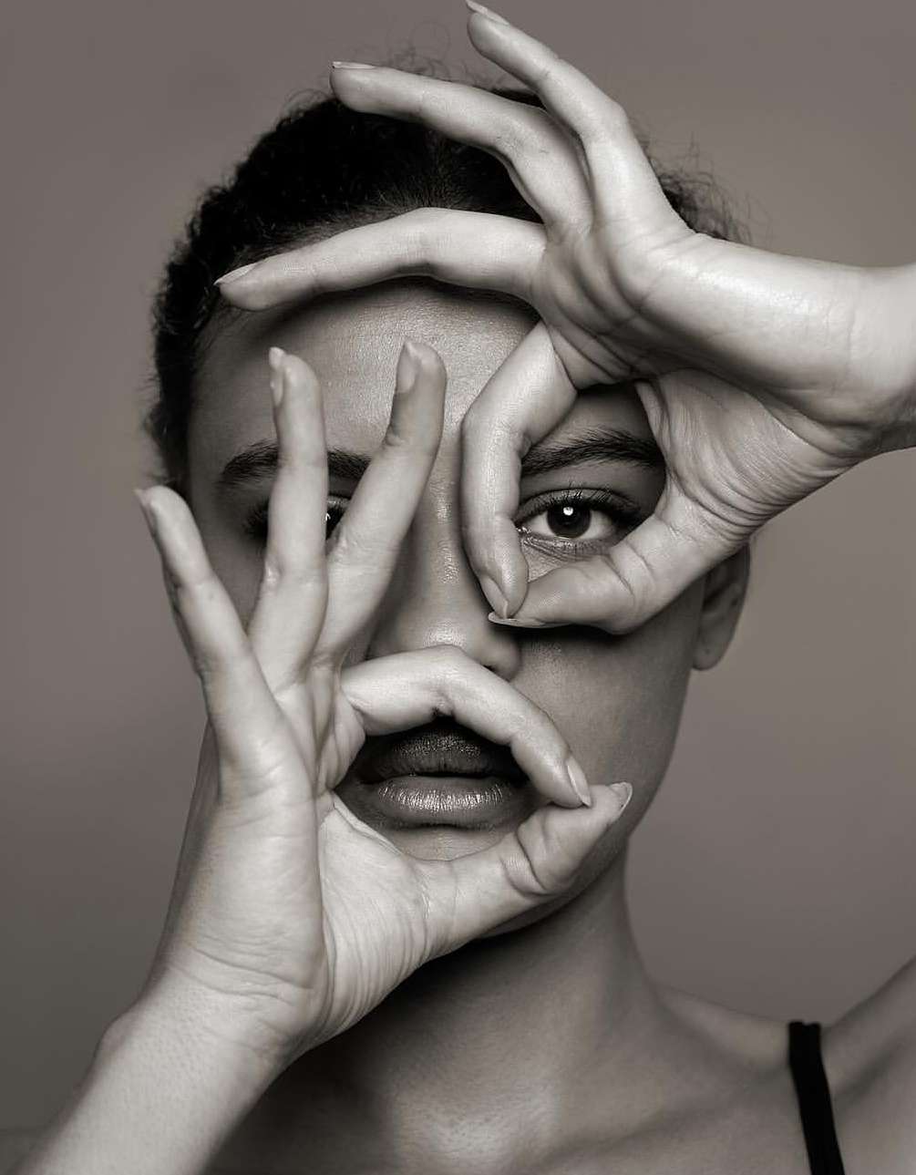 Monochrome portrait of a woman with hands framing her face in circular shapes against a grey background in a photo studio.