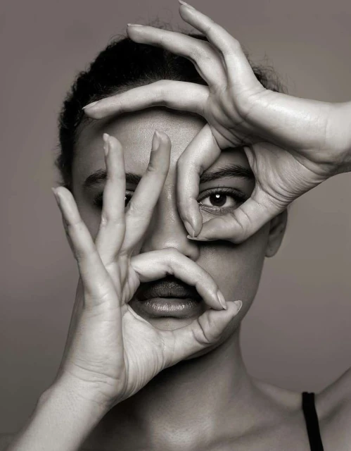 Monochrome portrait of a woman with hands framing her face in circular shapes against a grey background in a photo studio.