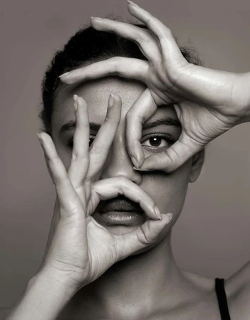 Monochrome portrait of a woman with hands framing her face in circular shapes against a grey background in a photo studio.