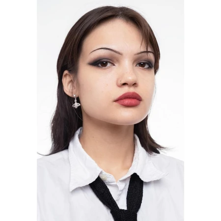 Close-up portrait of a woman with dramatic eye makeup, wearing a white shirt and black tie, set against a stark white backdrop.