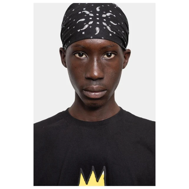 Close-up portrait of a person with dark skin wearing a patterned black bandana and a black t-shirt with a yellow crown graphic.