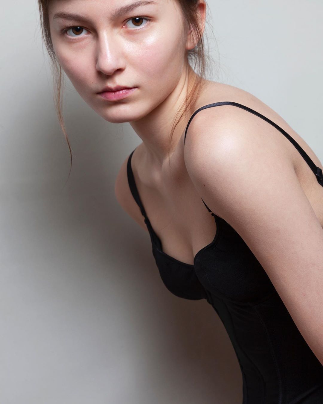 Portrait of a young woman with fair skin and light brown hair, wearing a black top, gazing at the camera in an indoor setting.