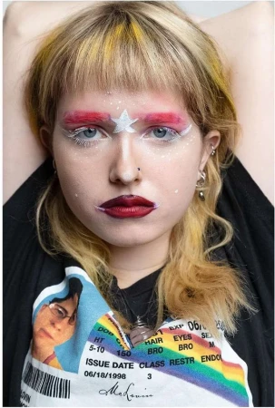 Portrait of a young woman with creative makeup featuring red brows, a star on her forehead, and a graphic t-shirt.