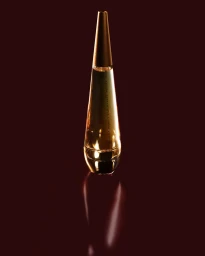 Cone-shaped glass perfume bottle with a tapered cap standing on a dark reflective surface