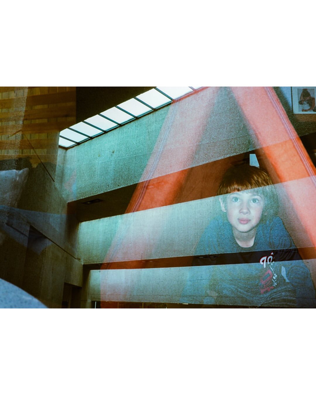 Young boy with red hair poses indoors with diffused light and a modern architectural background featuring teal, orange and white elements.