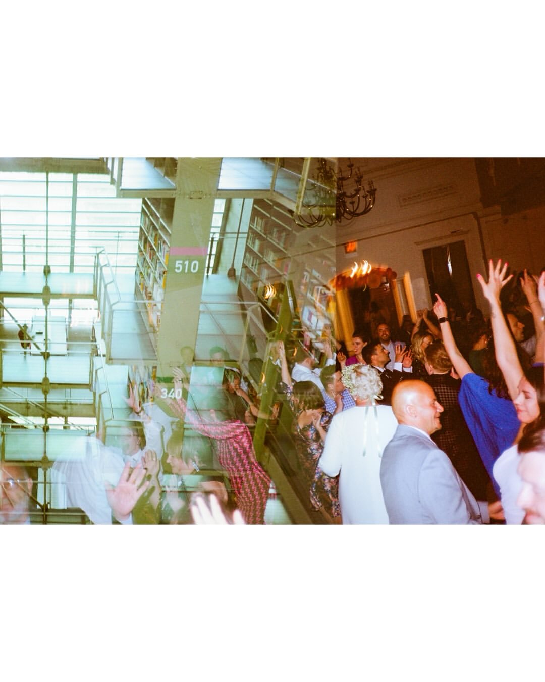 Wedding reception in a large hall with guests celebrating, including adults and children. Stairs are visible in the background.