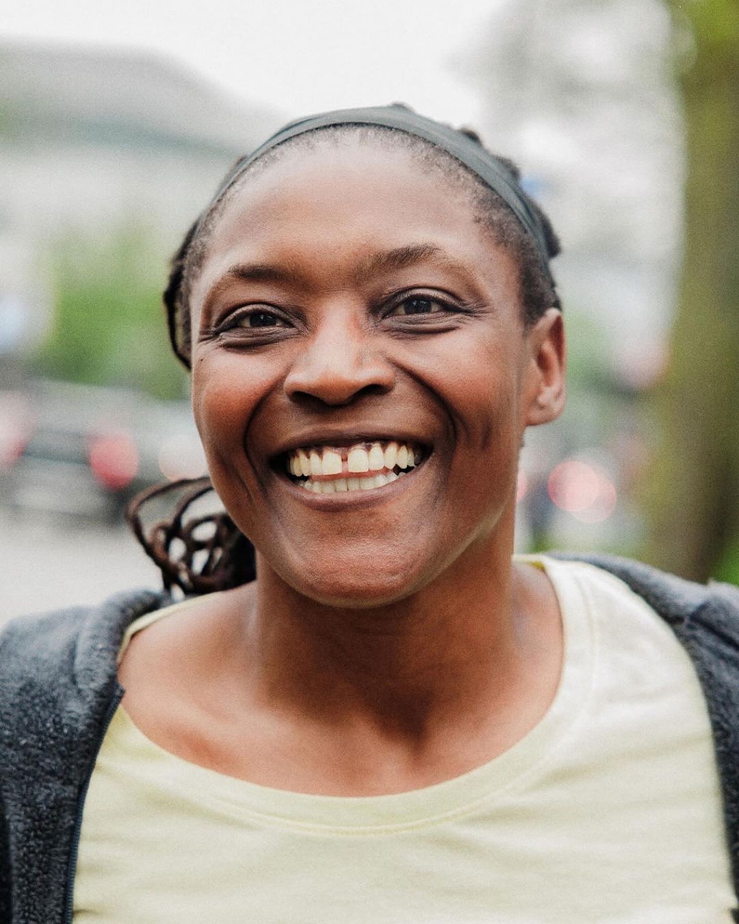 Close-up of a smiling African-American woman with a visible gap between her front teeth, wearing a yellow shirt and grey cardigan.