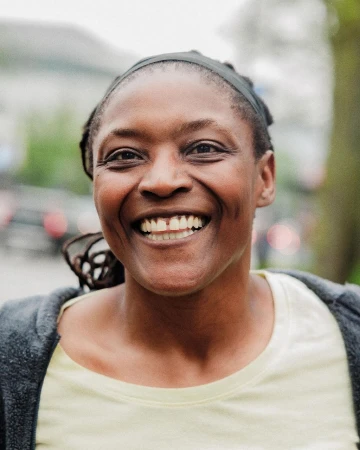 Close-up of a smiling African-American woman with a visible gap between her front teeth, wearing a yellow shirt and grey cardigan.