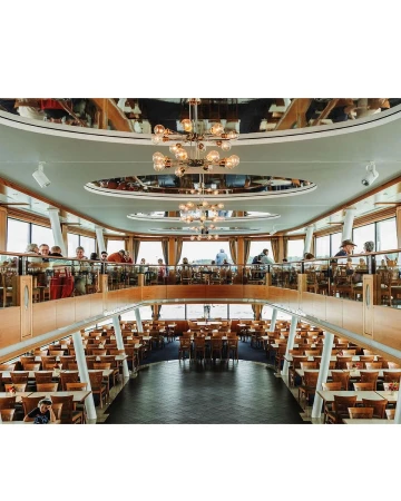 Two-story restaurant interior with rows of tables and chairs, visible patrons on the upper level, and modern chandeliers.
