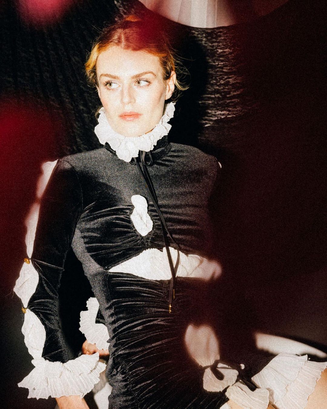 Elegant portrait of a woman with light skin, wearing a black mini dress with white ruffles, posing in a studio with soft lighting.