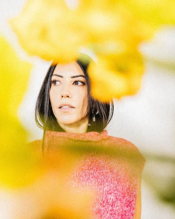 Portrait of a woman wearing a pink textured top framed by blurred yellow foreground flowers by photographer Stephanie Bassos.