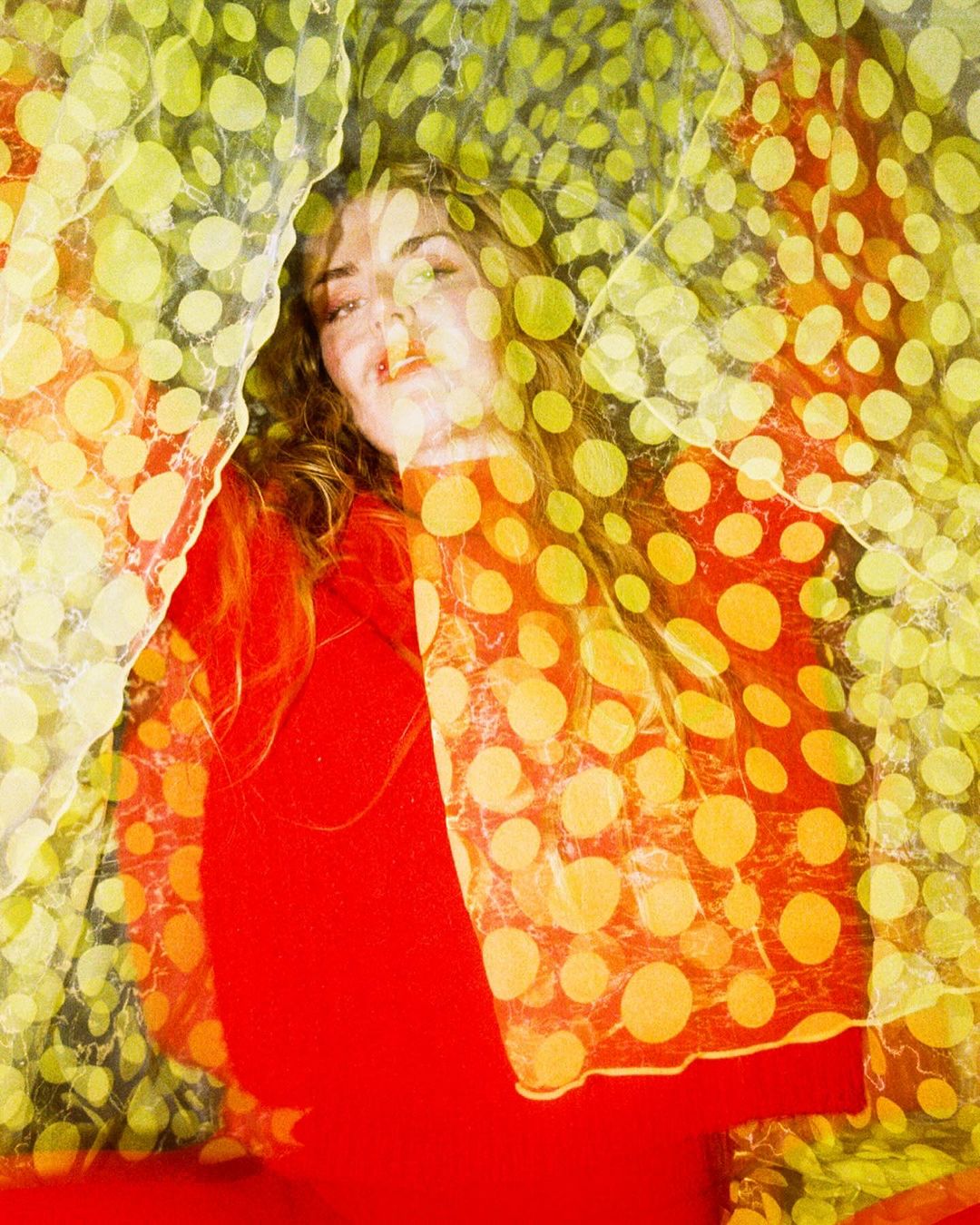 Adult female laying beneath polka dot fabric in a medium shot with warm studio lighting and red tones. Beauty and fashion concept.