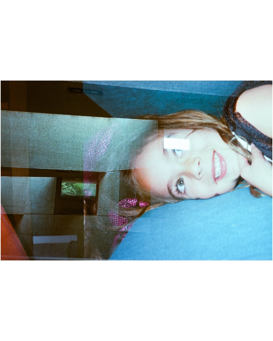Portrait of a smiling child with brown hair lying down, a window reflection with abstract shapes, and a teal surface in the frame.