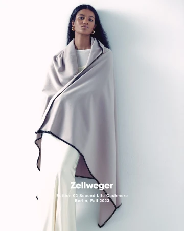 Model draped in a soft grey cashmere wrap with black trim standing against a white seamless background