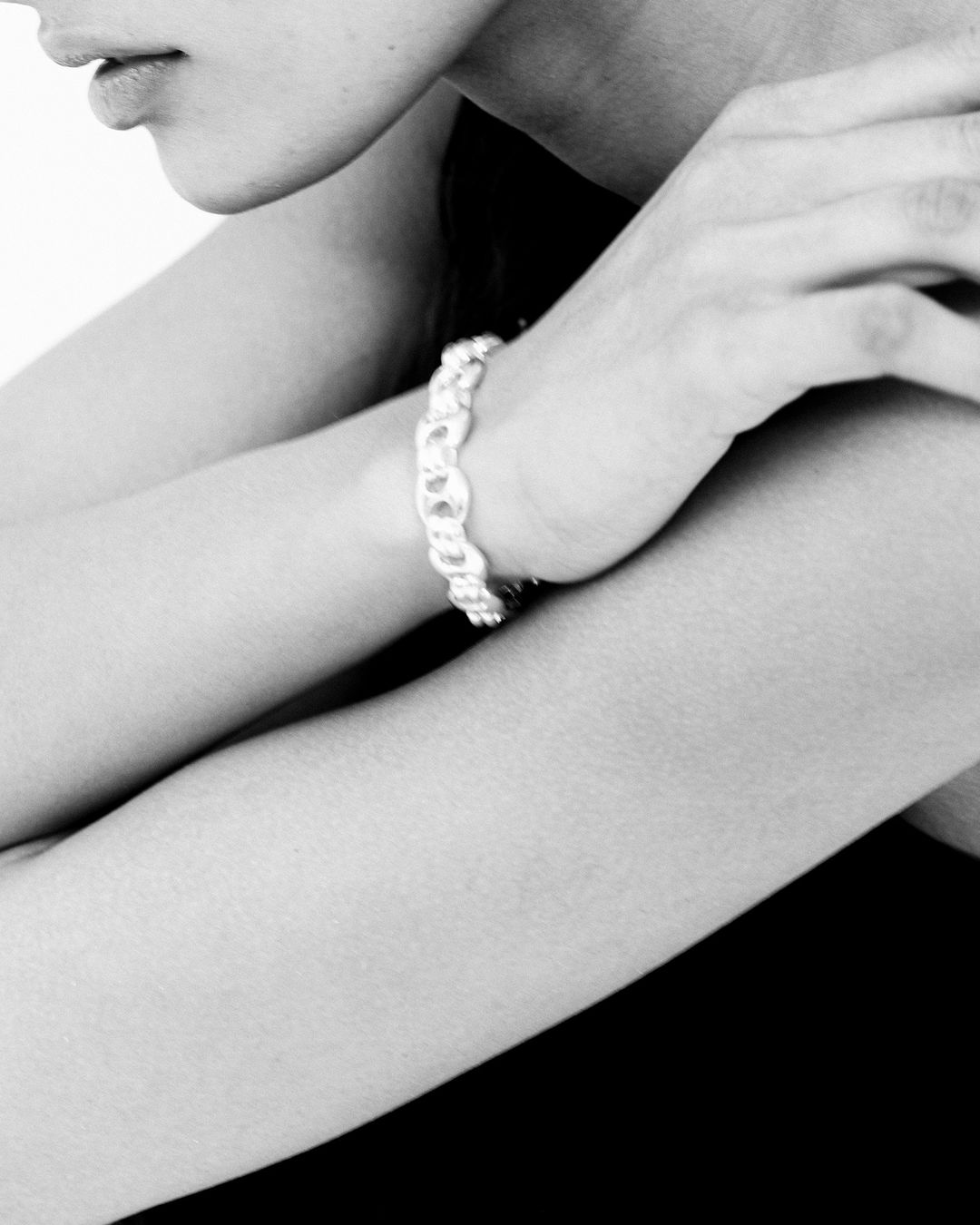 Close-up studio shot of a fair-skinned woman's hands and arms, adorned with a linked silver bracelet, against a dark neutral background.