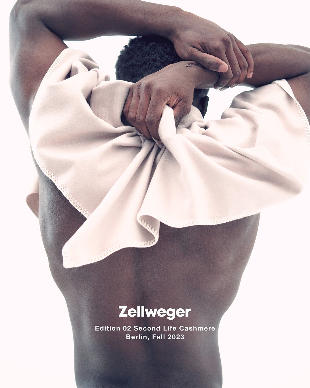 A Black male torso poses against a white background, draped with a soft beige textile, in a studio setting for a fashion editorial.