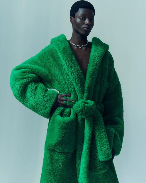 Fashion portrait of a Black man in a fluffy green bathrobe against a light background, showcasing style and texture in a studio setting.