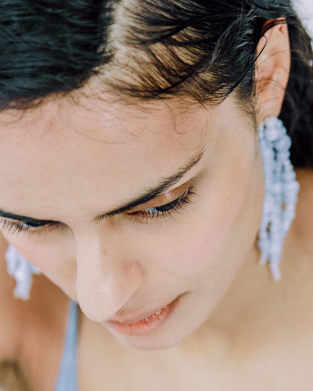 Close-up portrait of a woman wearing long beaded earrings and a blue top, photographed from above by Stephanie Pfaender in Paris.