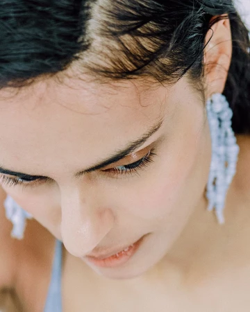Close-up portrait of a woman wearing long beaded earrings and a blue top, photographed from above by Stephanie Pfaender in Paris.