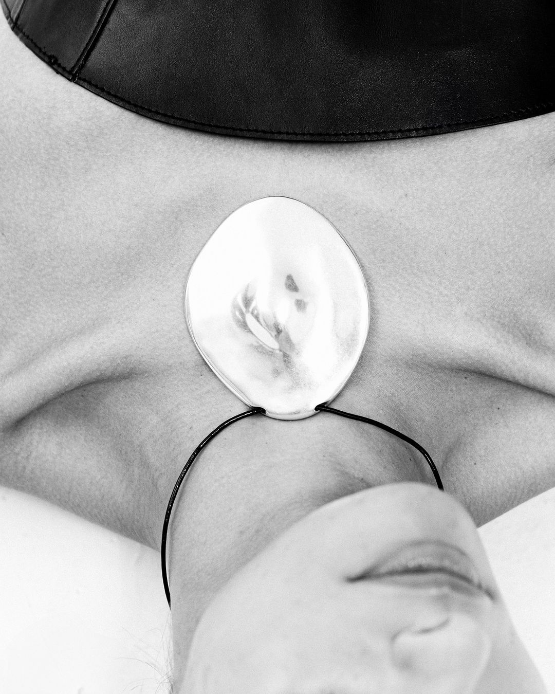 Close up portrait of a person wearing a large silver pendant necklace and a black collar against a white background