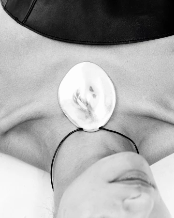 Close up portrait of a person wearing a large silver pendant necklace and a black collar against a white background