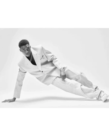 Monochrome portrait of a stylish young Black man in a suit striking a dynamic pose against a plain white background in a studio setting.