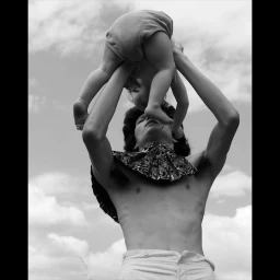 Monochrome low-angle shot of a person lifting a baby into the air against a cloudy sky