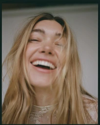Close up portrait of a smiling blonde woman looking down at camera against plain background