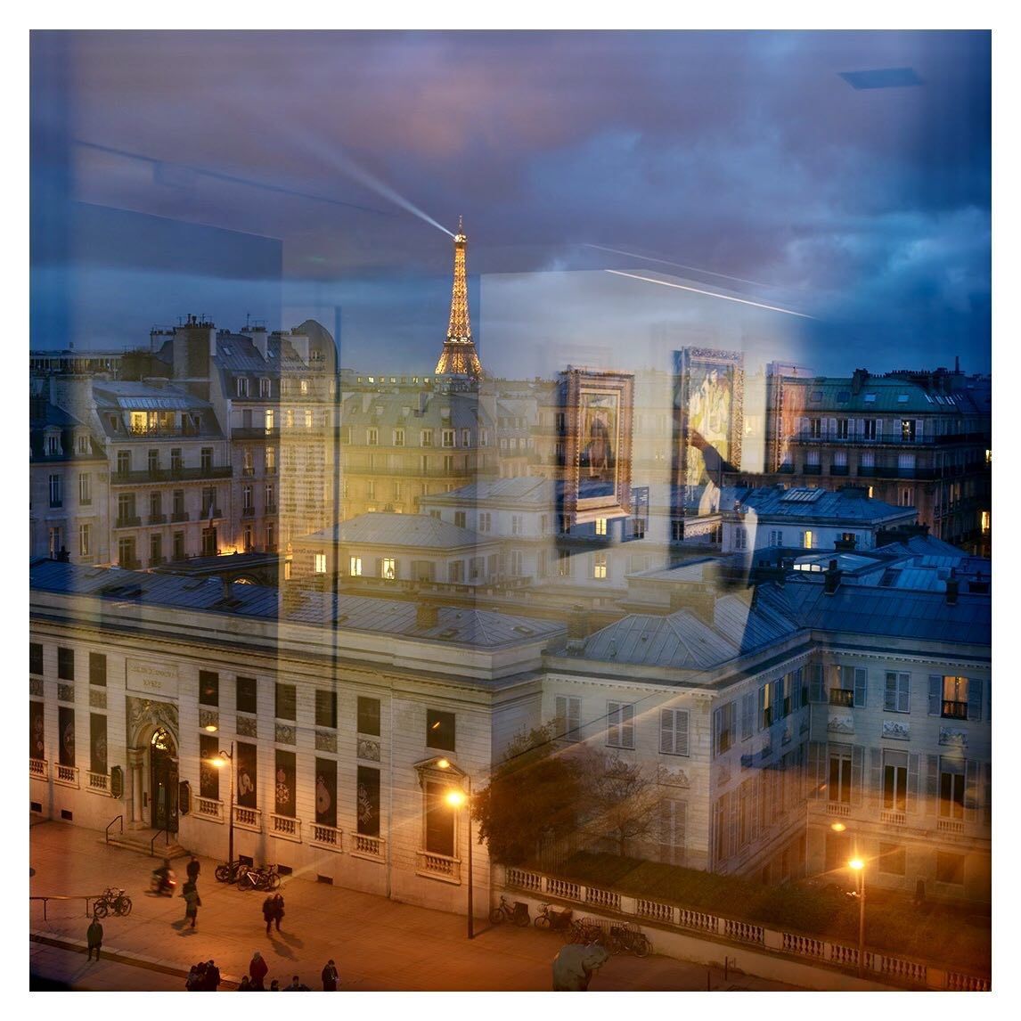 Paris cityscape at dusk featuring the illuminated Eiffel Tower and surrounding buildings, captured with reflections in a window.