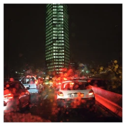 Night view of Paris traffic in the rain with a tall illuminated skyscraper and red taillights captured by Stephanie Tetu