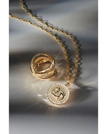 Gold necklace with round pendant and gold rings with engraved text on a gradient background. Jewellery still life close-up shot.