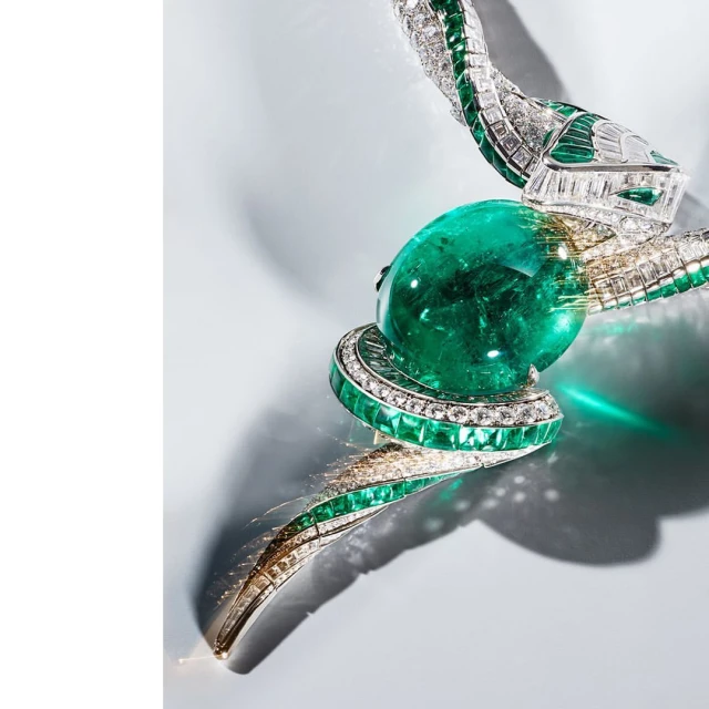 High-fashion jewelry shot: A snake-shaped necklace with white diamonds and emerald accents, coiled around a central emerald gem.