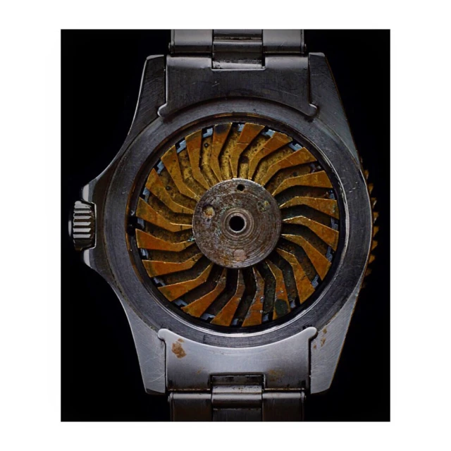 Close-up of a stainless steel wrist watch with a gold-colored, fan-shaped internal mechanism, set against a stark black background.